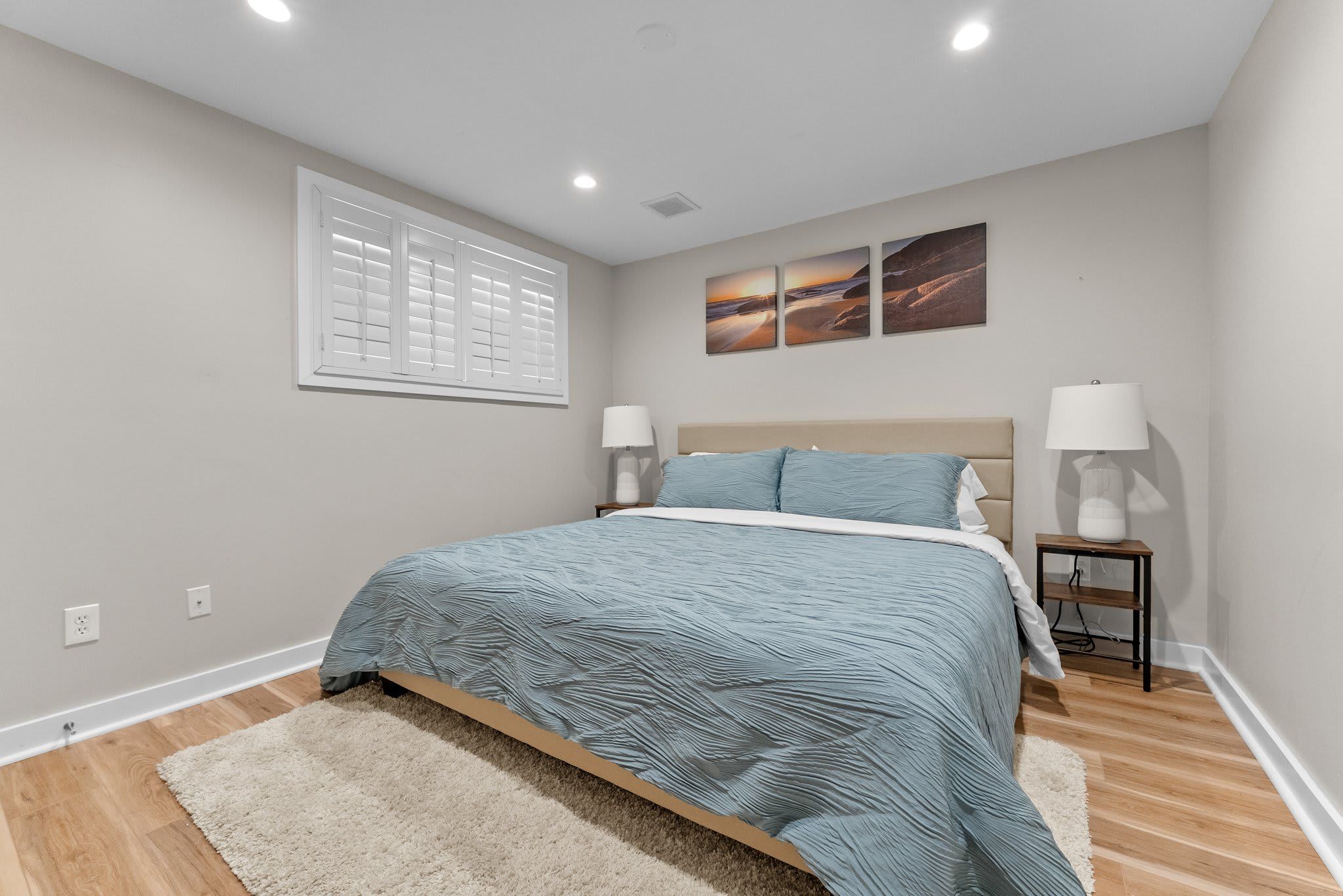 Quarto com cama, duas mesas de cabeceira, janela com persianas e três quadros na parede.
