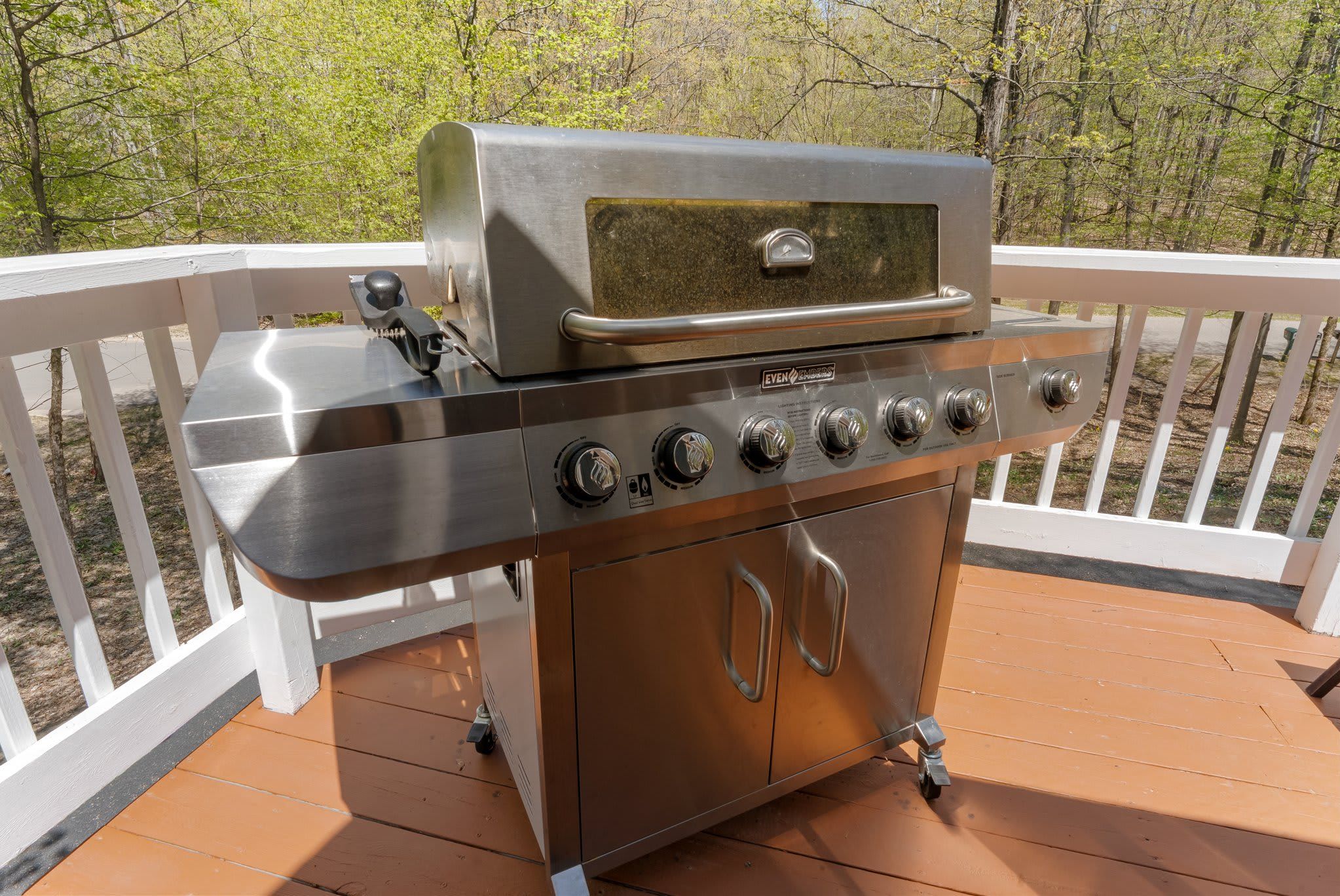 A stainless steel outdoor grill on a wooden deck with white railings.