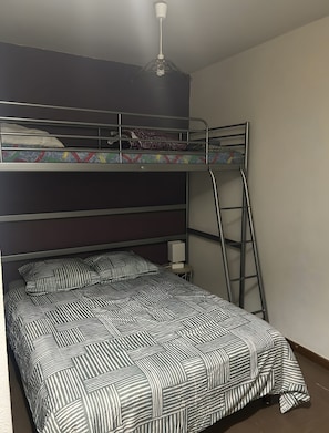 A bunk bed with a ladder, a bedside table with a lamp, and a ceiling light fixture.