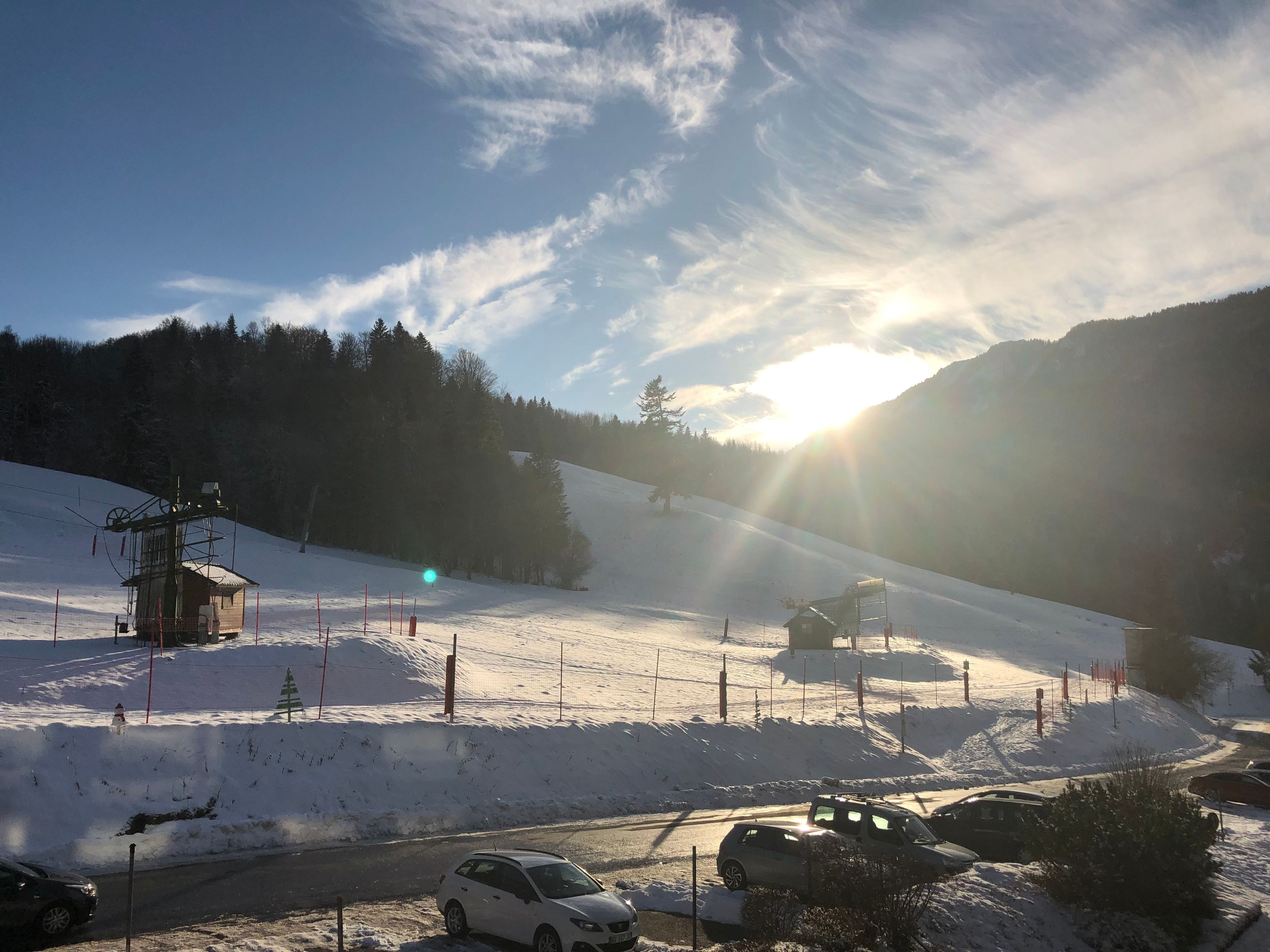 Pista da sci innevata con una seggiovia, una piccola baita e auto parcheggiate.