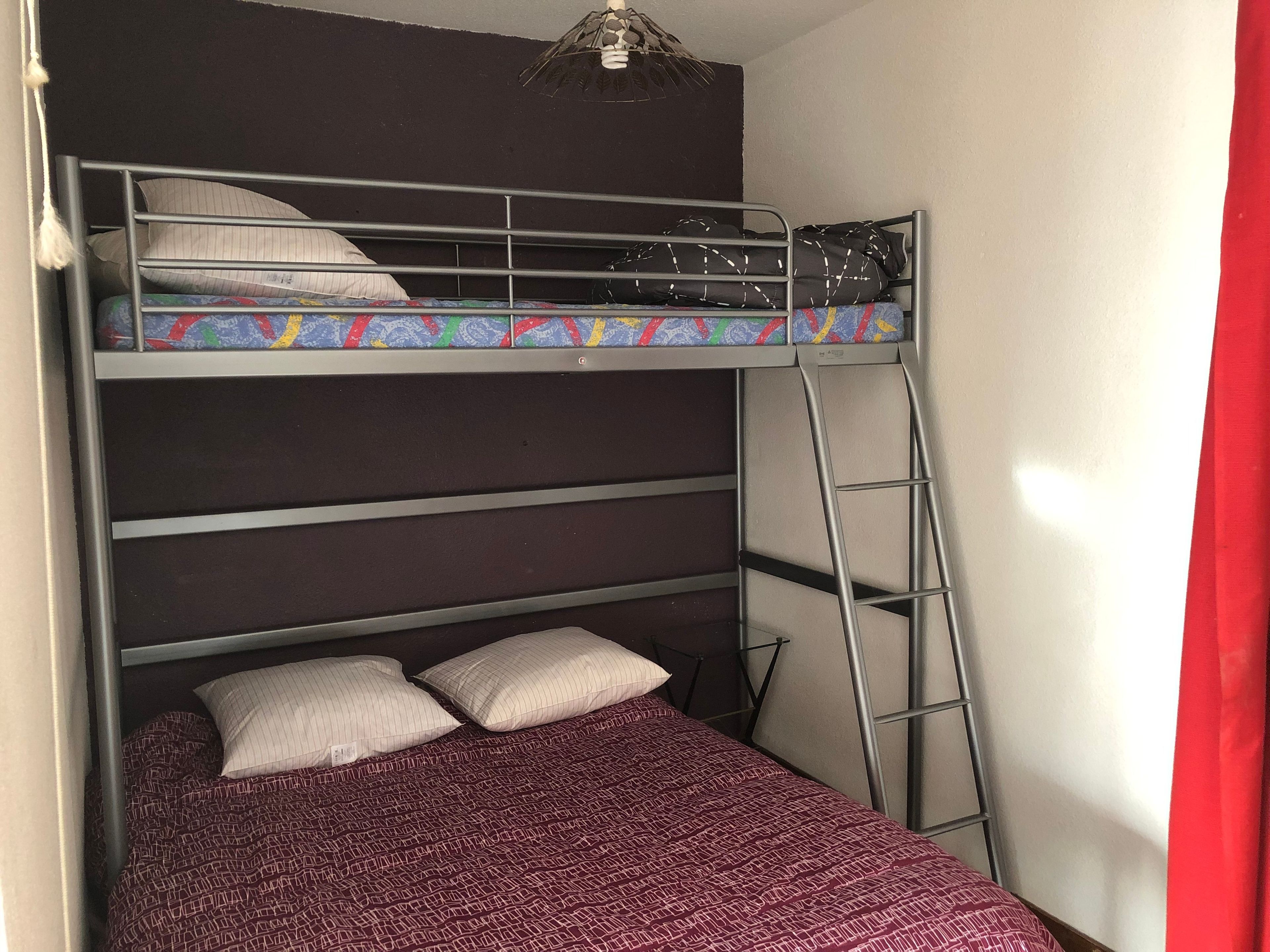 Een stapelbed met een ladder, twee kussens en een bedspreide met dessin.