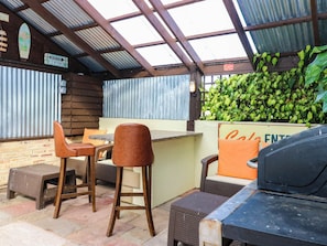 An outdoor patio area with a grill, bar stools, and a sign indicating a cafe entrance. - Calendonia Hut (Berwick-upon-Tweed)