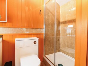 A bathroom with a white toilet, a glass-enclosed shower, and wooden paneling. - Calendonia Hut (Berwick-upon-Tweed)