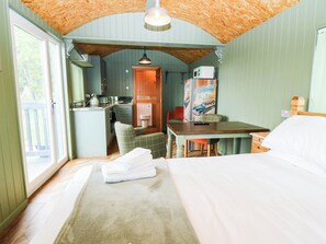 A room with a bed, a table, a chair, a kitchenette, and a view of the outdoors. - Calendonia Hut (Berwick-upon-Tweed)