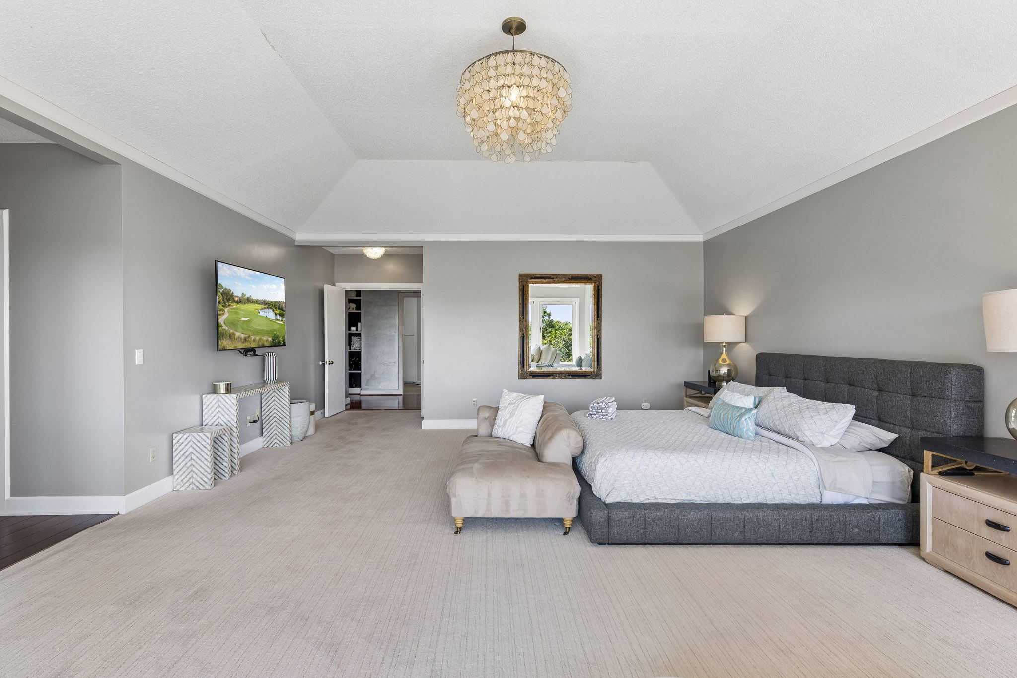 A spacious bedroom with a large bed, a television, a chandelier, and a view of a golf course.