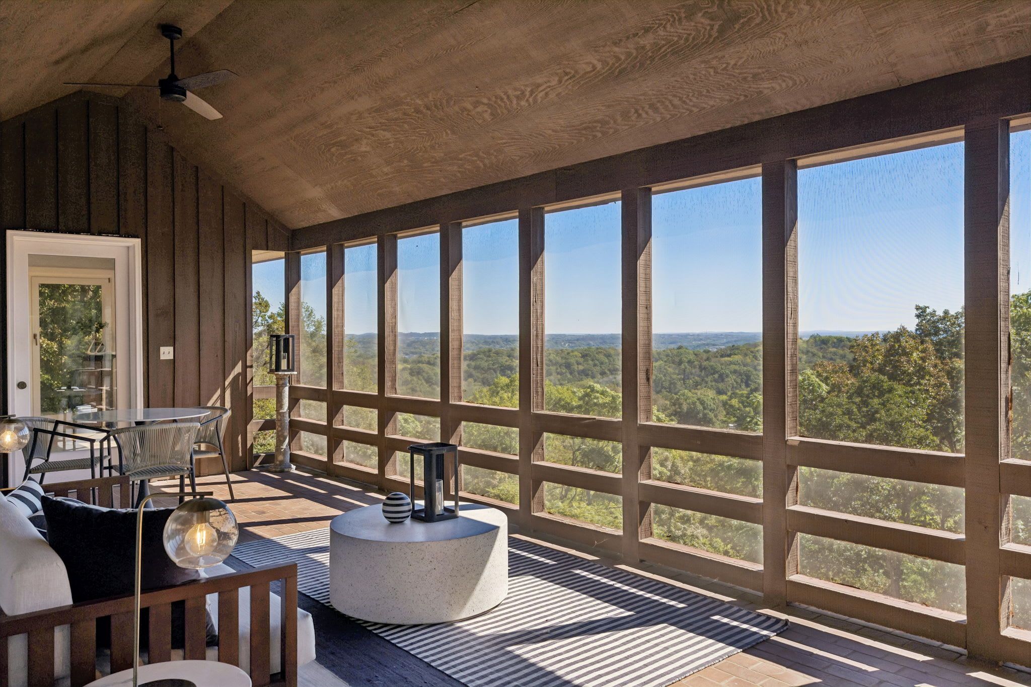 A spacious room with large windows, a wooden ceiling, and a view of a forested landscape.