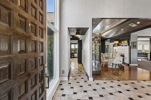 A hallway with a patterned floor, a wooden door, and a view into a dining area with chairs and a table. - Breathtaking mountain-view home w/ exclusive pool! (Goodlettsville)
