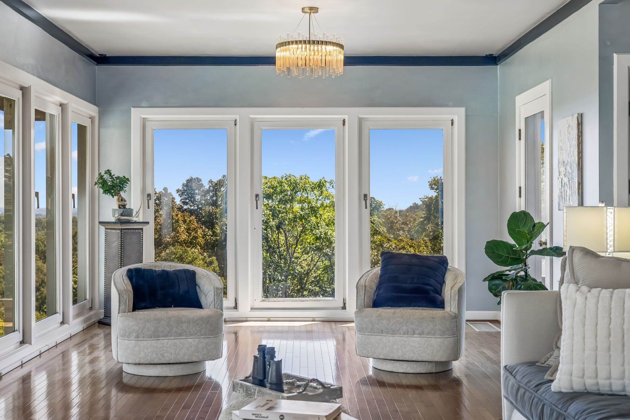 A spacious room with a large window, a chandelier, and two armchairs with cushions.