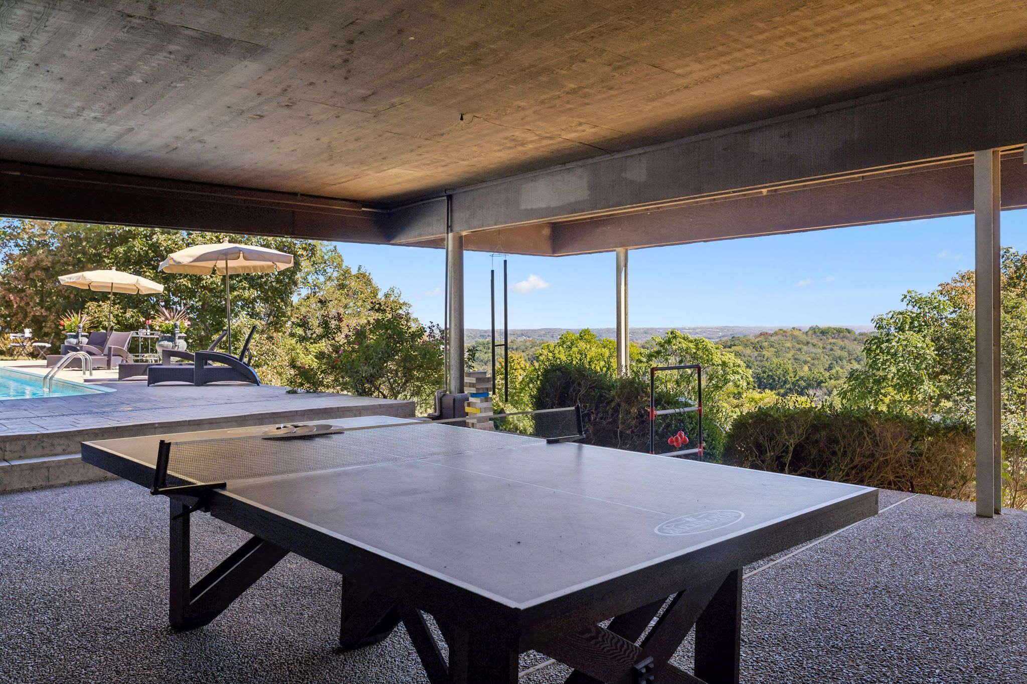 A ping pong table in an outdoor area with a view of a pool and greenery.