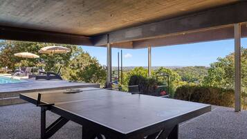 A ping pong table in an outdoor area with a view of a pool and greenery.