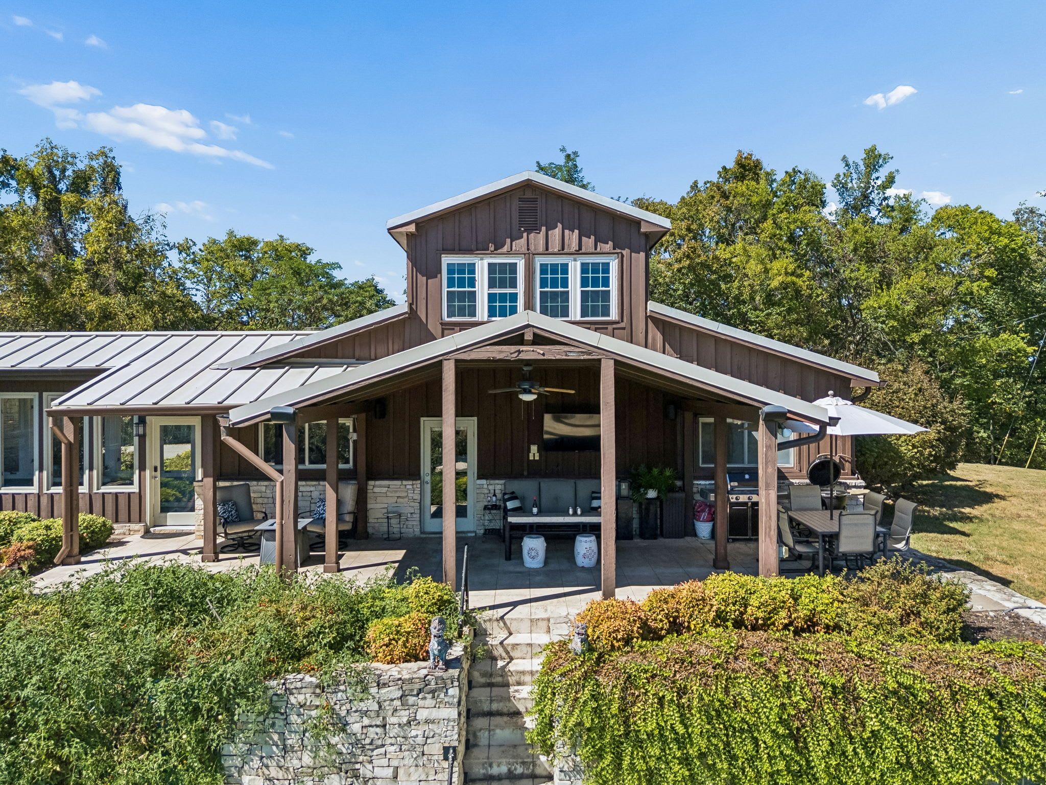 A two-story house with a covered porch, stone steps, and outdoor seating.