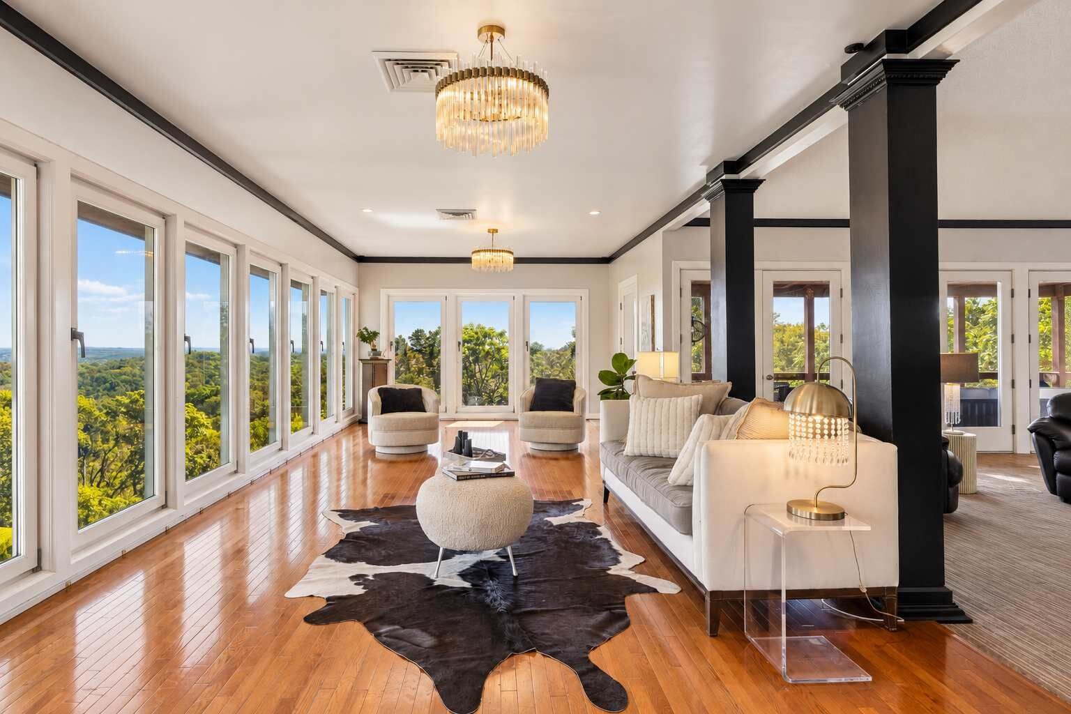 A spacious room with large windows, a wooden floor, a black and white rug, and modern furniture.