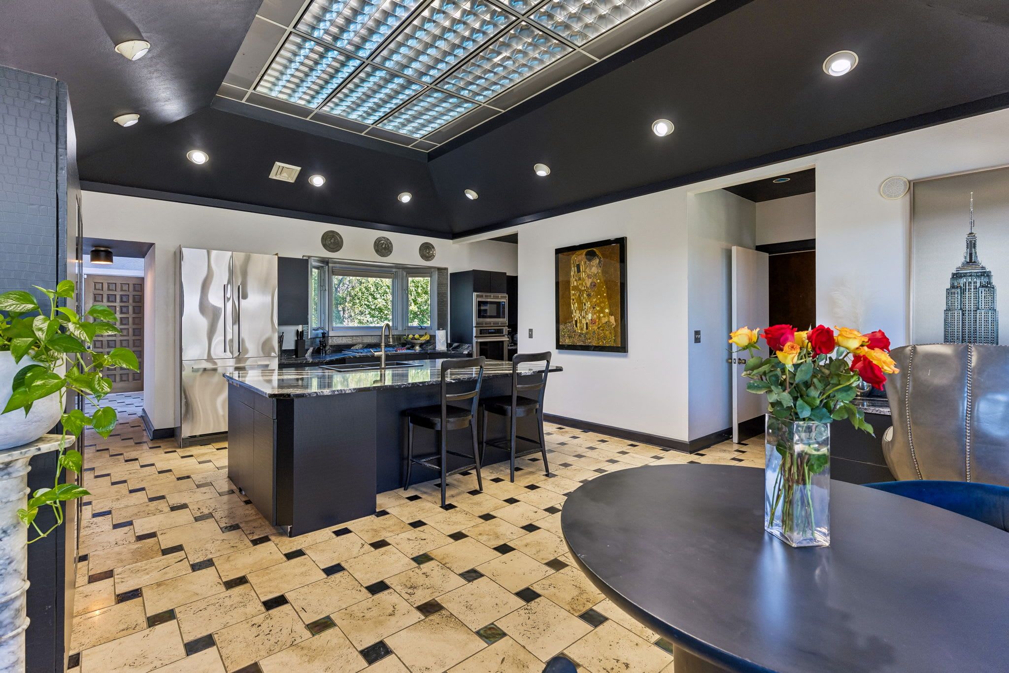 A modern kitchen with a central island, a dining area with a round table, and a living space with a sofa and a vase of flowers.
