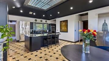 A modern kitchen with a central island, a dining area with a round table, and a living space with a sofa and a vase of flowers.