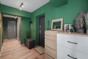 A modern interior with a green wall, a wooden floor, a desk with drawers, a mirror, a Buddha statue, and a telephone. - Lumina 2BR Apart w/ Parking I Center (Łódź)