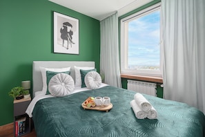 A neatly made bed with a green bedspread, pillows, and a tray with fruits and drinks. - Lumina 2BR Apart w/ Parking I Center (Łódź)
