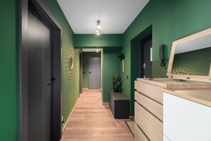 Un couloir avec un plancher en bois, des murs verts, une porte noire et un bureau avec un miroir.