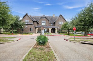 A large, two-story building with a symmetrical facade, a central entrance with an arched doorway, and a stop sign to the right. - Bring the group! Comfort-First Cottage Living (College Station)