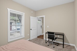 A bedroom with a bed, a desk, and a door leading to another room. - Bring the group! Comfort-First Cottage Living (College Station)