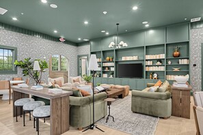 A modern living room with a flat-screen TV, green sofas, a coffee table, and a bookshelf filled with books and decorative items. - Aggieland Stay with Pool and  Perfect for Game Days (College Station)