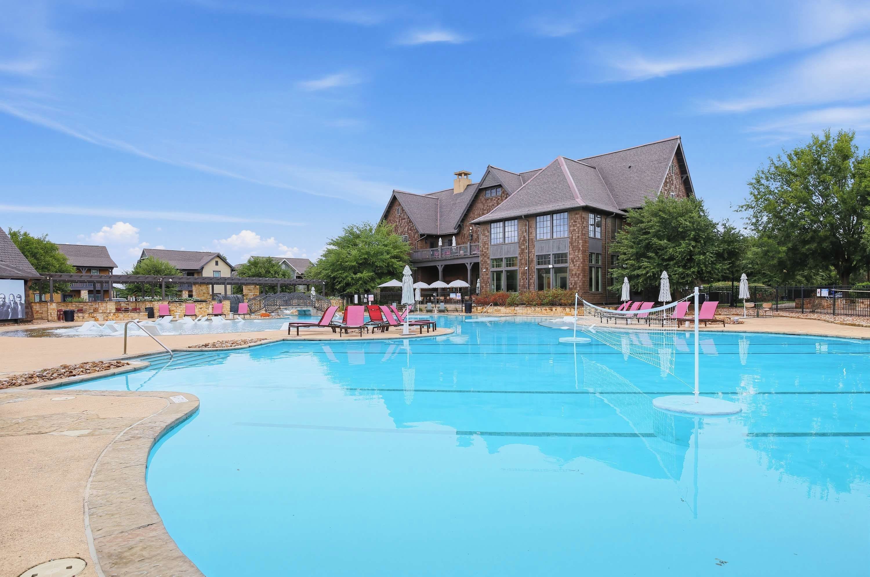 A swimming pool with lounge chairs and umbrellas, surrounded by a building with a stone facade and a large window.