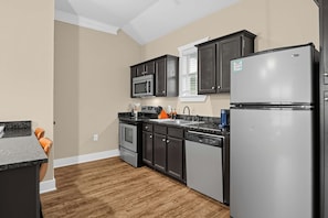 A modern kitchen with dark cabinetry, stainless steel appliances, and a wooden floor. - Aggieland Stay with Pool and  Perfect for Game Days (College Station)