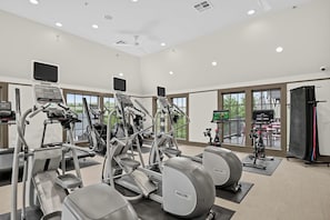 A gym with various exercise machines, large windows, and a ceiling fan. - Game Day Getaway Near Texas A&M with Pool (College Station)