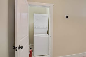 A laundry room with a washer and dryer, a fire extinguisher, and a thermostat on the wall. - Game Day Home Base with Pool and Near Texas A&M (College Station)