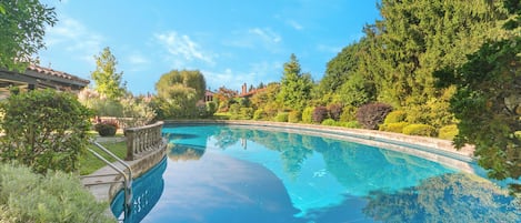 A clear swimming pool surrounded by lush greenery and a well-maintained garden.