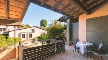 Un patio esterno coperto con pavimento in mattoni, un tavolo con sedie e vista su un edificio con un camino.