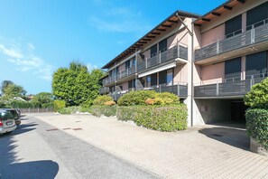 A multi-story residential building with balconies, a paved driveway, and parked cars. - Borgo Della Motta Swimming Pool &golf (Travedona-Monate)
