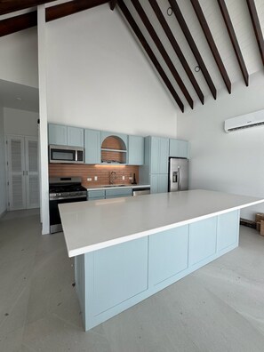 A modern kitchen with a central island, light blue cabinets, a stainless steel refrigerator, and a built-in microwave. - Pwani House (San Pedro)