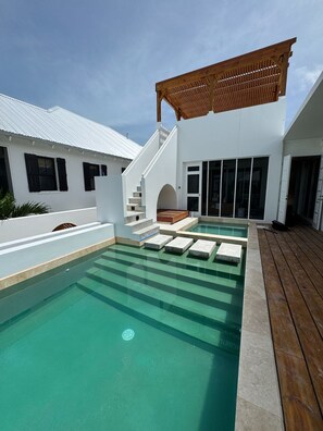 A modern outdoor swimming pool with a wooden deck, a covered seating area, and a staircase leading to a second level. - Pwani House (San Pedro)