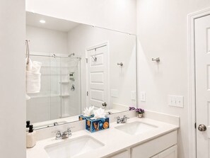 Une salle de bain moderne avec un grand miroir, deux lavabos et une douche.