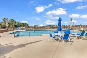 A swimming pool with blue chairs and umbrellas, surrounded by a fence and trees. - Brand New 3BR Home - Sleeps 10 - Pool Access (Myrtle Beach)