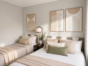 Une chambre d’hôtel avec deux lits, une table de chevet avec une lampe et trois œuvres d’art abstraites accrochées au mur.