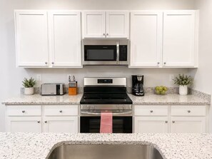 A kitchen with white cabinets, a microwave, a stove, a toaster, a coffee maker, and a sink. - Brand New 3BR Home - Sleeps 10 - Pool Access (Myrtle Beach)