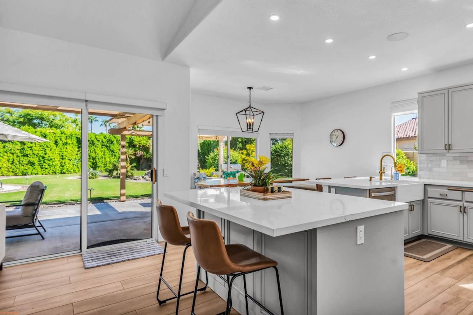 A modern kitchen with a large island, bar stools, and a view of a lush garden.