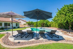 A backyard with a swimming pool, lounge chairs, and a large umbrella. - La Quinta Desert Escape | Private Pool | Monthly Stay (La Quinta)