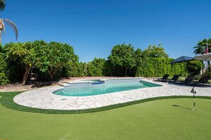 Piscina com borda de pedra, rodeada por grama verde e árvores.