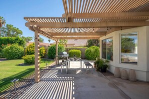 Ein überdachter Patio-Bereich mit Grill, Sitzgelegenheiten und Blick auf einen Swimmingpool.