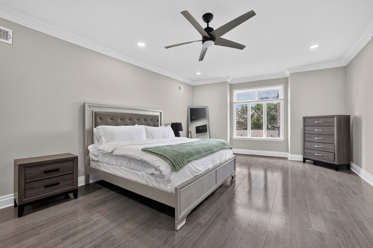A bedroom with a bed, nightstands, a dresser, a ceiling fan, and a window.