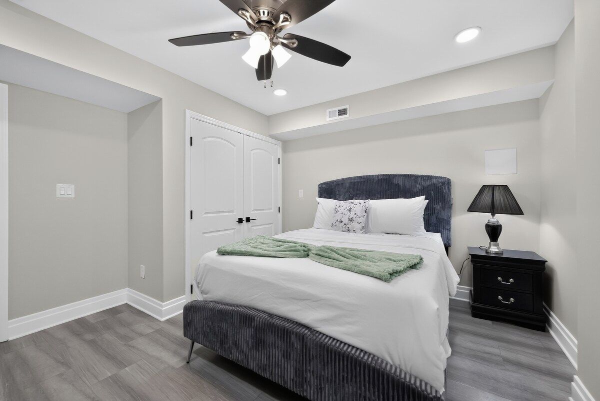 A bedroom with a bed, a nightstand, a ceiling fan, and a door.