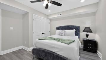 A bedroom with a bed, a nightstand, a ceiling fan, and a door.