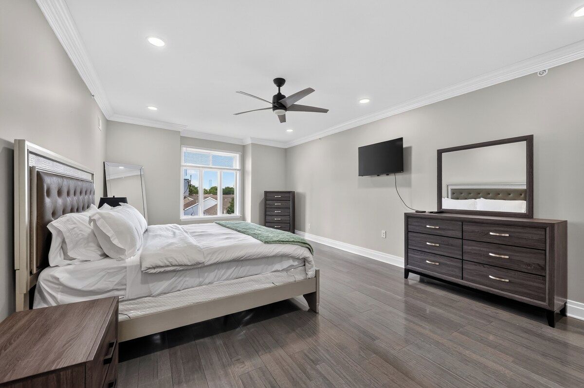 A bedroom with a bed, a dresser, a television, and a ceiling fan.