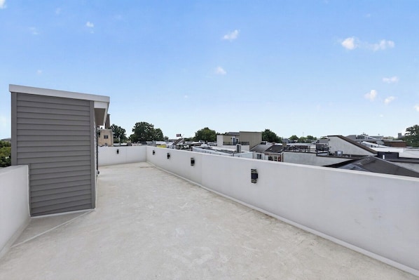A rooftop terrace with a flat roof, white walls, and a grey building on the left.