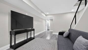A modern living room with a flat-screen TV on a black stand, a grey sofa, and a patterned rug.