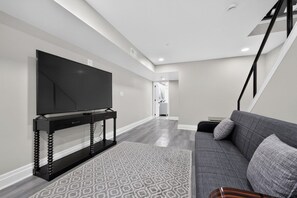 A modern living room with a flat-screen TV on a black stand, a grey sofa, and a patterned rug. - Luxury Queens Village - 4Br 4.5Ba - Rooftop Patio (Philadelphia)