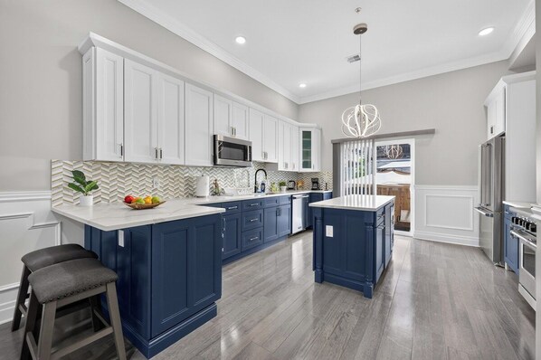 A modern kitchen with white upper cabinets, blue lower cabinets, a central island, and a stainless steel refrigerator.
