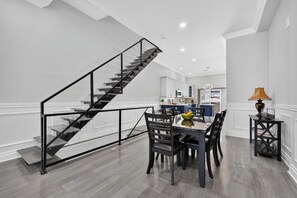 A modern kitchen with white cabinetry, a dining area with a table and chairs, and a staircase with a glass railing.